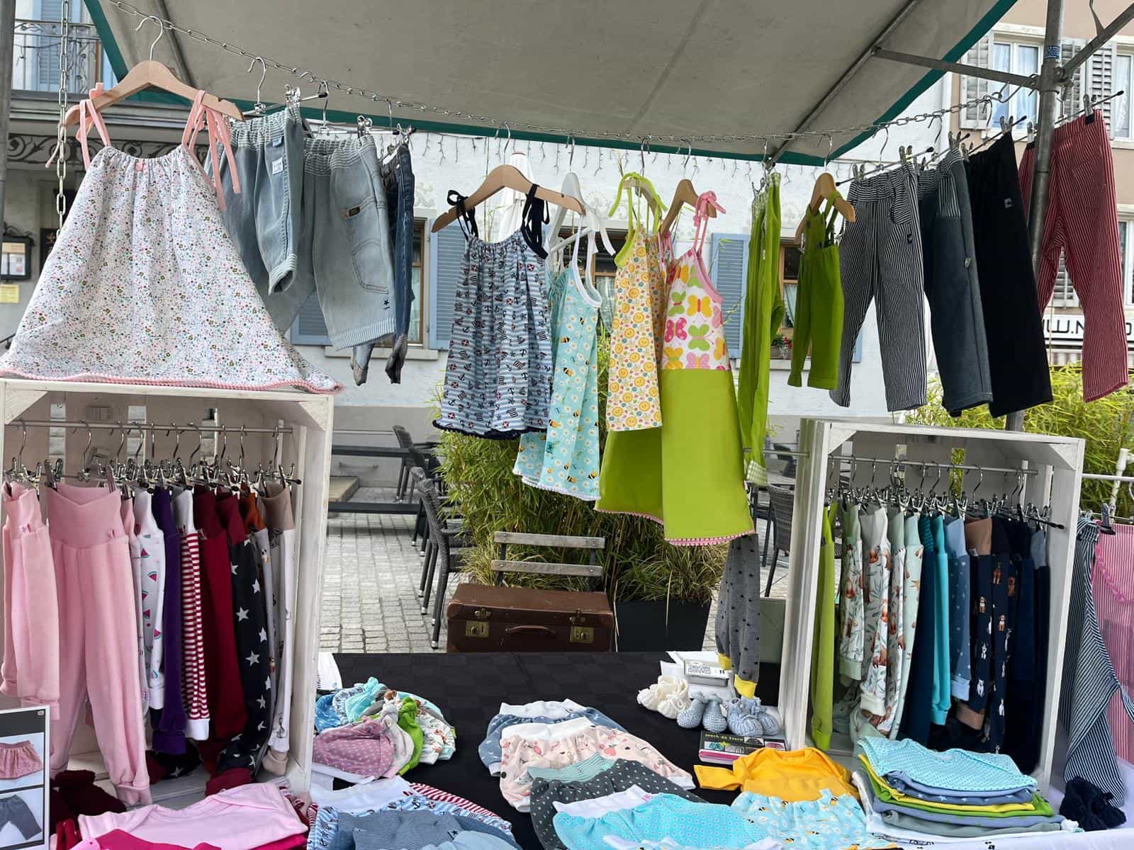 Marktstand unter dem Zeltdach mit aufgehängten Sommerkleidern und Hosen